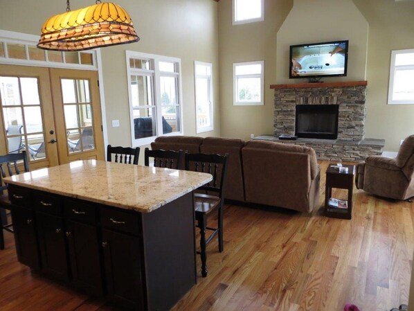 A spacious living room with a stone fireplace, a large TV mounted above it, and a cozy seating area with a sofa and recliner.