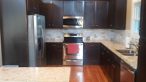 A kitchen with dark wooden cabinets, stainless steel appliances, a granite countertop, and a window with curtains.