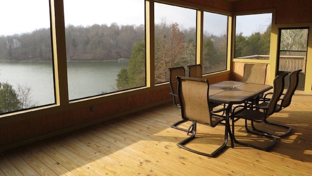 A spacious room with a large table and chairs, large windows offering a view of a lake and trees, and a ceiling fan.