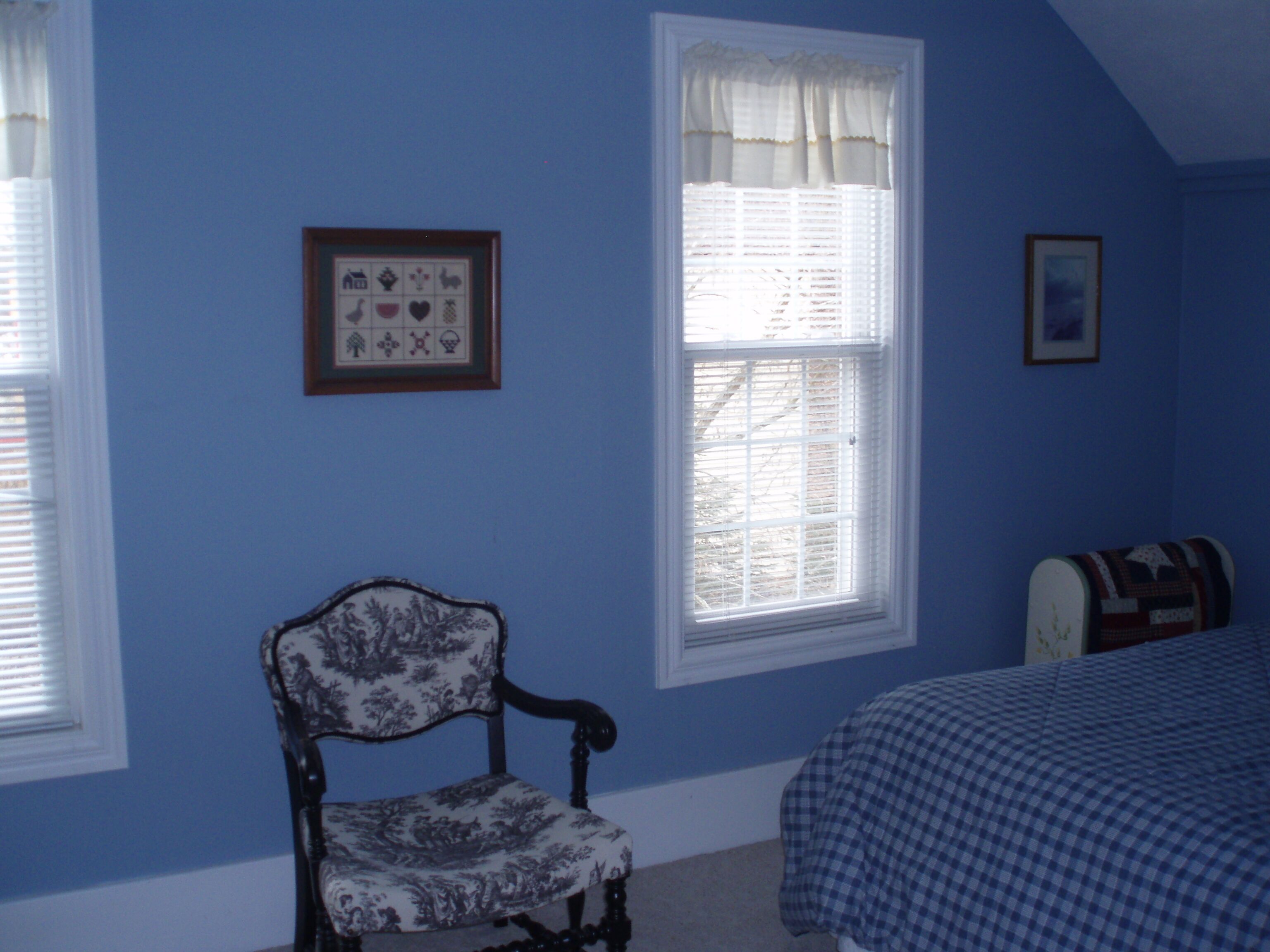 A bedroom with a single bed, a chair, a window with blinds, and a framed picture on the wall.