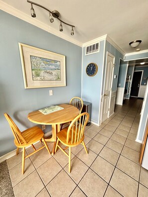 Un comedor con una mesa y sillas de madera, un cuadro en la pared, un reloj y una puerta que da a otra habitación.