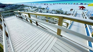 A wooden boardwalk leading to a beach with umbrellas and people.