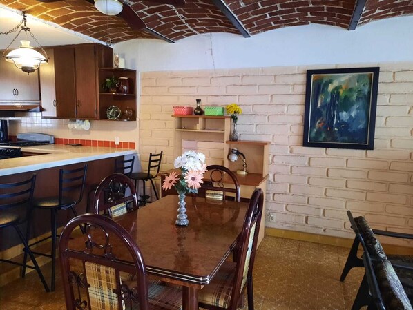Une cuisine avec un mur en briques, des meubles de rangement en bois, une table à manger avec des chaises et un tableau accroché au mur.