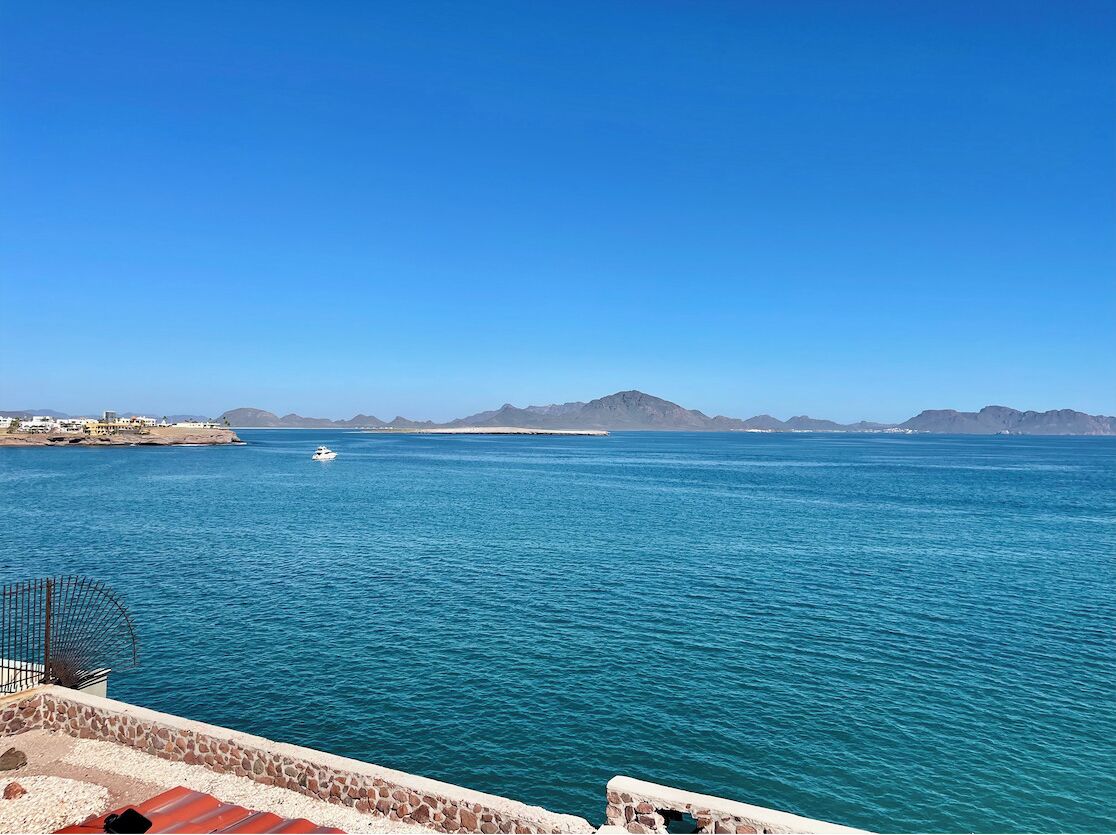 Une vue sur la côte, avec un ciel bleu dégagé, une mer calme et des montagnes à l’horizon.