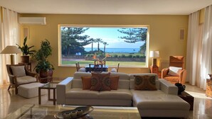 A living room with a large window, a sofa, a glass coffee table, and a view of the ocean. - Private villa in exclusive area, with pool, tennis and direct  access to beach (Marbella)