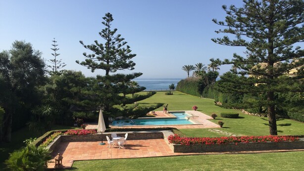 A pool area with a view of the ocean, surrounded by well-maintained lawns and trees. - Private villa in exclusive area, with pool, tennis and direct  access to beach (Marbella)