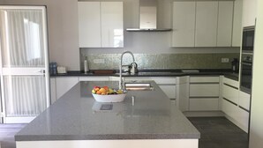 A modern kitchen with a central island, white cabinets, a stainless steel sink, and a tiled backsplash. - Private villa in exclusive area, with pool, tennis and direct  access to beach (Marbella)