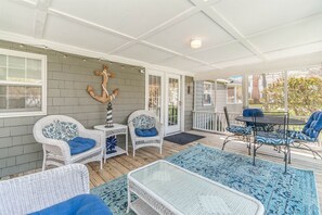 Une véranda couverte, meublée de meubles en osier, agrémentée d’une ancre décorative et offrant une vue sur l’extérieur.