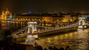 Ein Nachtblick auf eine Brücke mit beleuchteten Lichtern, einen Fluss und historische Gebäude im Hintergrund.