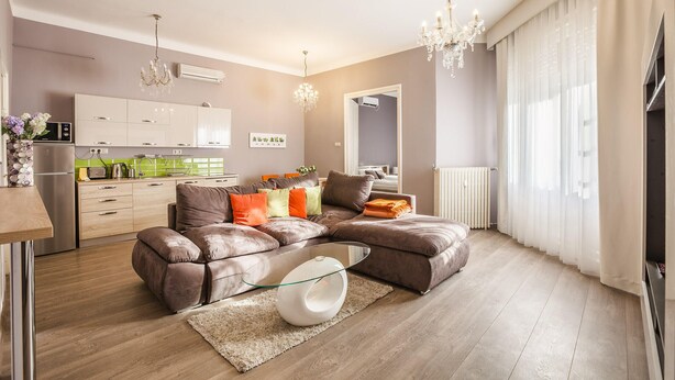 Ein modernes Wohnzimmer mit einer Eckcouch, einem Glastisch und einer Kronleuchter.