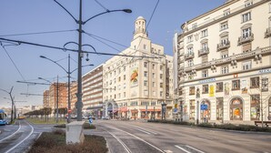 Eine Straße mit Straßenbahnschienen, ein Gebäude mit Kuppel und ein Gebäude mit der Aufschrift 'ALEXANDRA'.