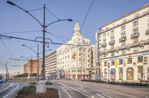 A street with tram tracks, a building with a dome, and a building with a sign that says "ALEXANDRA".