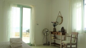 Une chambre à coucher comprenant un lit, une chaise, un bureau avec un miroir, un ventilateur et une vue sur l’extérieur.