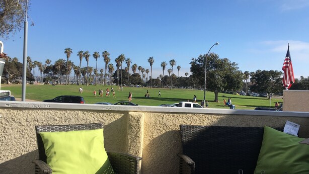 A patio area with wicker furniture and a view of a park with palm trees and people. - Steps to the water on both sides!! (San Diego)