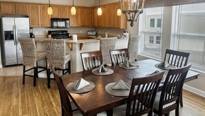 Une cuisine moderne avec des meubles en bois, un réfrigérateur en acier inoxydable, un four à micro-ondes et une machine à café. On y trouve des chaises en osier disposées autour d’une table à manger en bois, agrémentée de sets de table.