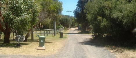 A rural road with a gravel surface, surrounded by trees and a fence.