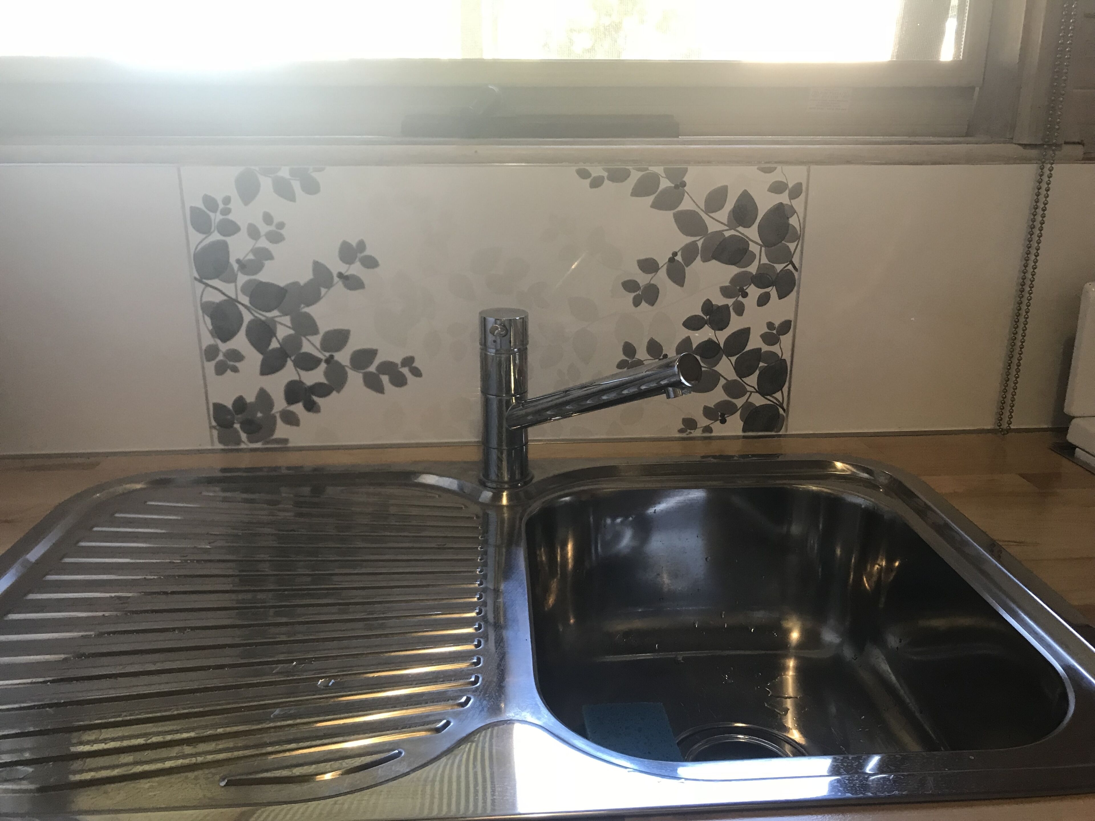 Un lavamanos de acero inoxidable con un grifo moderno y un escurreplatos.
