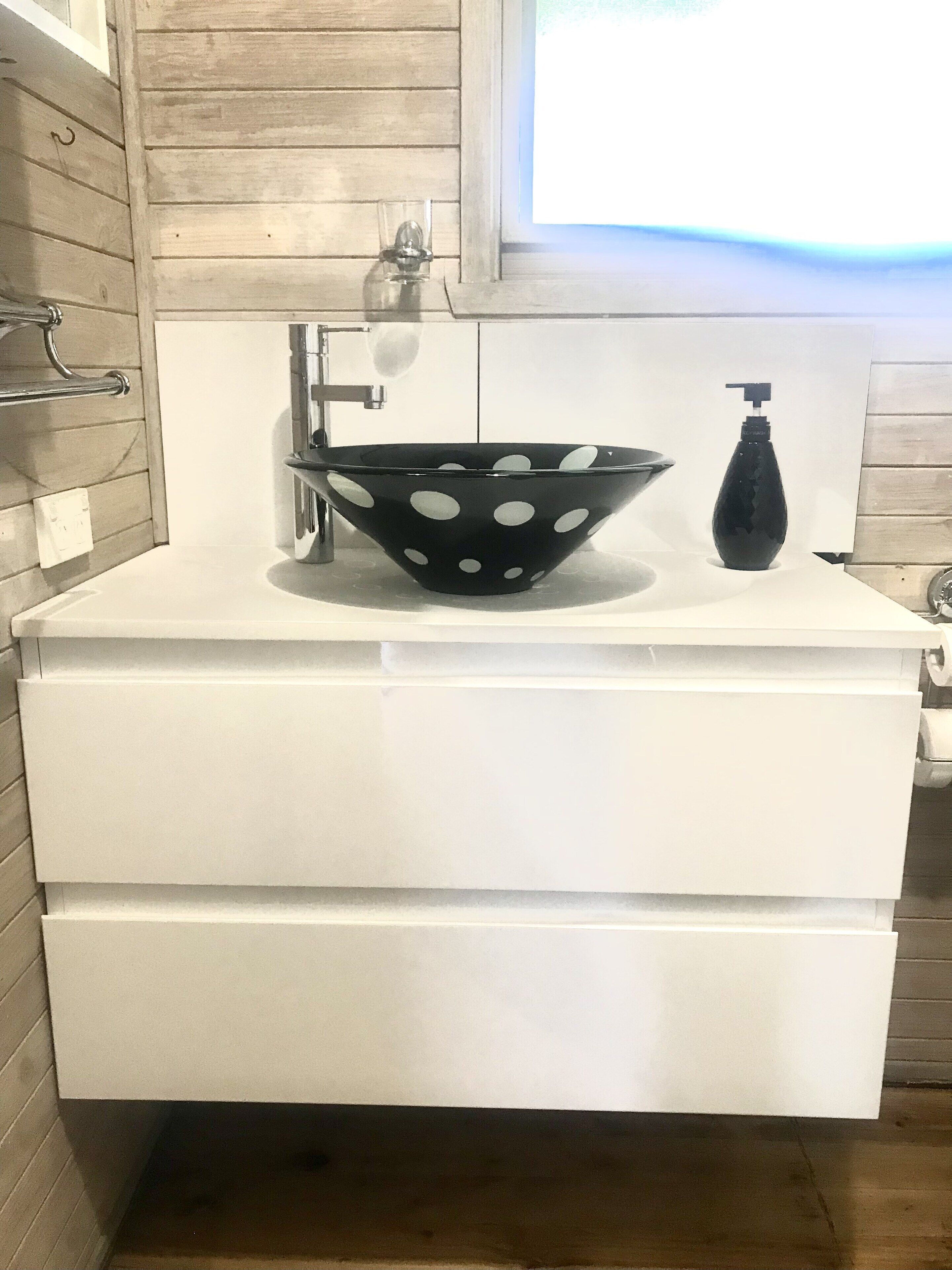 Un bagno con un mobile vanitario bianco, un lavabo nero con pois bianchi, un dispenser per sapone nero e una finestra sopra il lavabo.