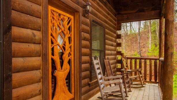 A wooden cabin with a porch featuring rocking chairs and a decorative wooden door. - Hole in the Wall: 🐾Pet friendly, Mountain View, Game Room, Hot Tub🌲 (Sevierville)