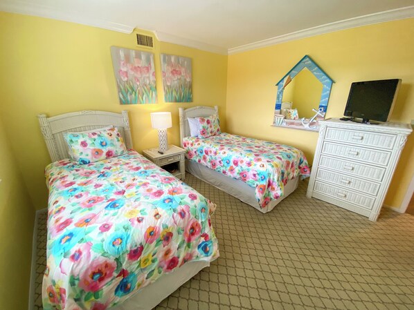 Une chambre avec deux lits, une commode et des œuvres d’art accrochées au mur.