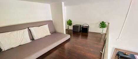 A modern living room with a grey sofa, a small table with a decorative item, and a wooden floor.
