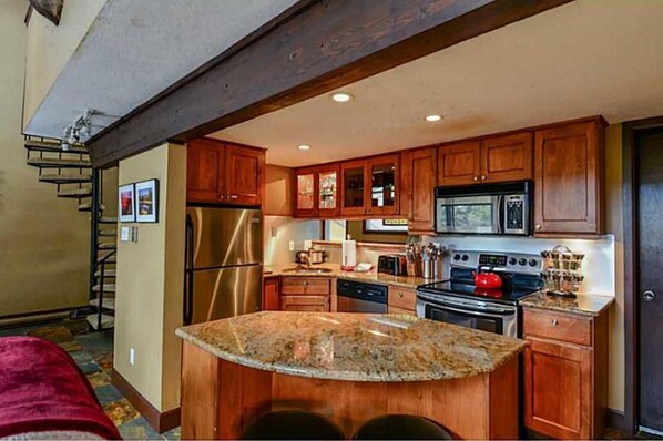 Kitchen features a central island with a granite countertop, stainless steel appliances, and wooden cabinets with glass doors.