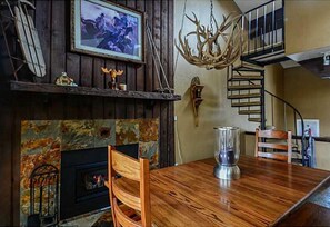 Enjoy meals in this cozy dining area with a fireplace, metal pitcher, and wooden table.