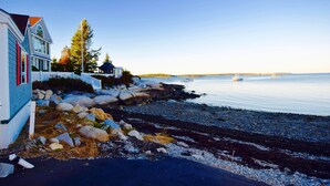 A coastal property with a white fence, a blue building, and a view of the sea. - Lobster Bill - Spruce Head Island, USA (South Thomaston)