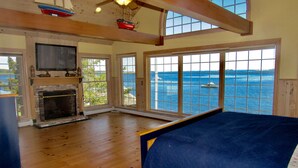 A spacious bedroom with a large bed, a fireplace, and a view of the sea through large windows. - Lobster Bill - Spruce Head Island, USA (South Thomaston)