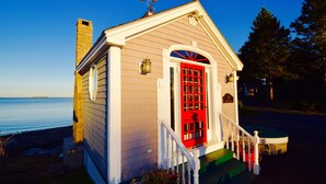 A small, single-story building with a red door and white trim, located near a body of water. - Lobster Bill - Spruce Head Island, USA (South Thomaston)