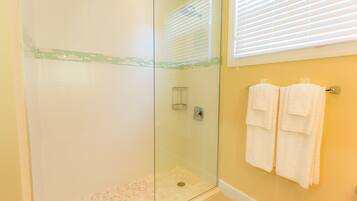 A glass-enclosed shower with a tiled floor, a towel rack with two towels, and a window with blinds.