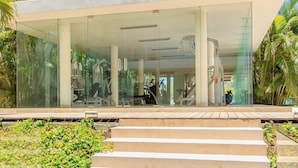 A modern building with glass walls, a covered outdoor area, and exercise equipment visible inside. - Family Friendly Beachside Condo with Pool & Gym (Playa del Carmen)