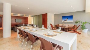 A modern dining area with a long table set for six, a television mounted on the wall, and a painting of a bird in flight. - Family Friendly Beachside Condo with Pool & Gym (Playa del Carmen)