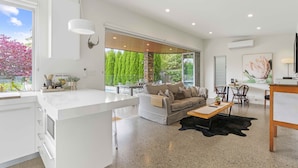 Een moderne leefruimte met keuken, eethoek en zithoek met uitzicht op groen.