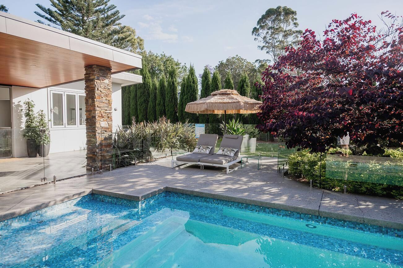 A modern house with a swimming pool, stone pillar, and a thatched umbrella.