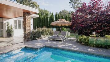 A modern house with a swimming pool, stone pillar, and a thatched umbrella.