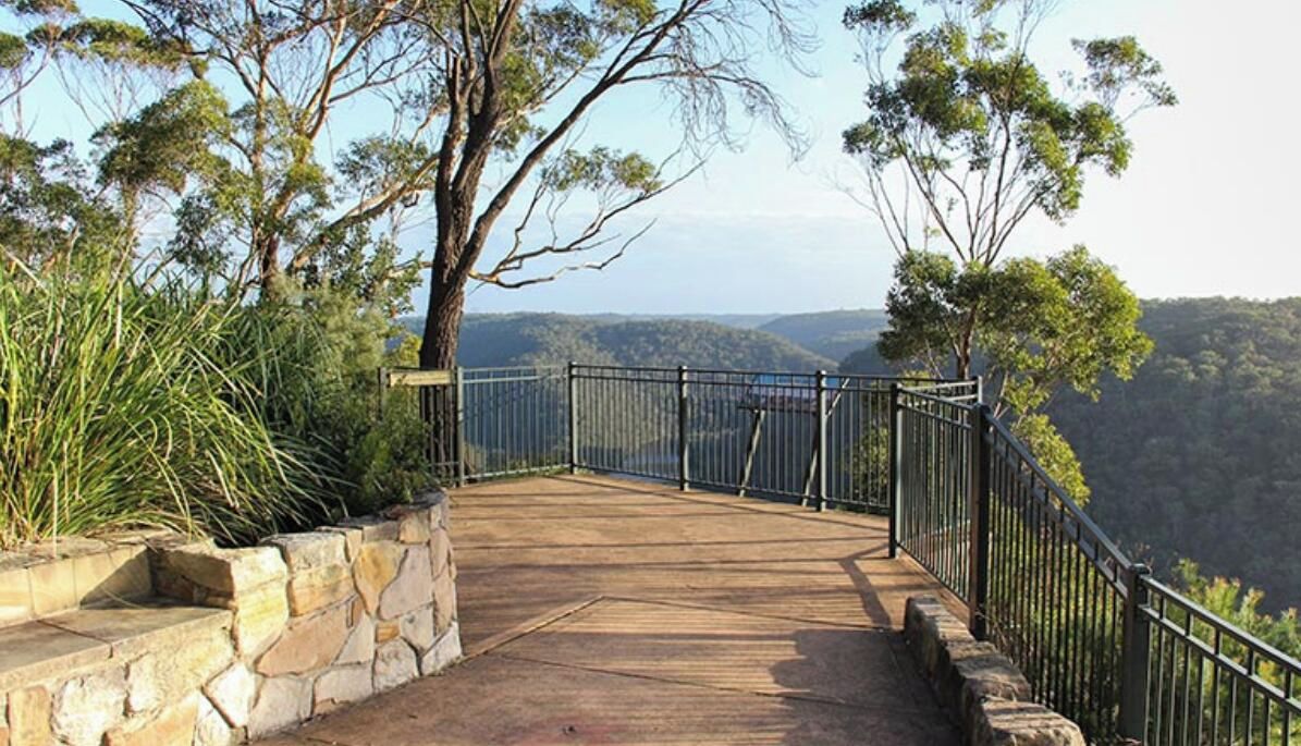 A wooden deck with stone steps leading to a railing overlooking a scenic landscape.