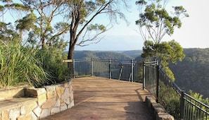 Un sendero pavimentado con escalones de piedra y barandillas de metal, rodeado de árboles y con vistas a un paisaje montañoso.