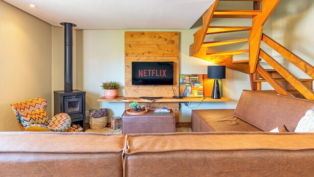 Una sala de estar acogedora con chimenea, un letrero de Netflix, una escalera de madera y una zona de estar cómoda.