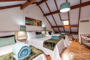 Um quarto amplo com duas camas, vigas de madeira, uma janela grande e um quadro na parede.