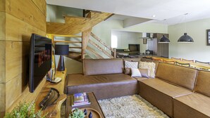 Una sala de estar moderna con un sofá de cuero marrón, una escalera de madera y una cocina al fondo.