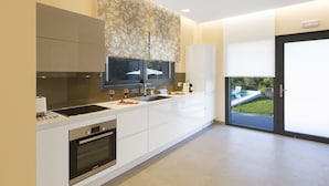 A modern kitchen with a built-in oven, a large island with a sink, and a view of a backyard with a pool. - Dione, Modern Private Villa With Swimming Pool (Corfu)