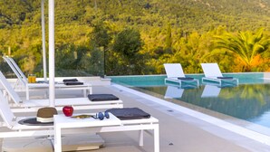 A poolside area with lounge chairs, a table with a hat, sunglasses, and a red apple. - Dione, Modern Private Villa With Swimming Pool (Corfu)