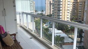 A balcony with a wooden bench, a white cabinet, and a view of high-rise buildings. - CONDOMINIUM CLUB (RESORT) RIVIERA 4 ROOMS - ALL TIME (Bertioga)