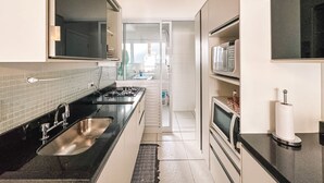 A modern kitchen with a black countertop, stainless steel sink, and a microwave. - CONDOMINIUM CLUB (RESORT) RIVIERA 4 ROOMS - ALL TIME (Bertioga)