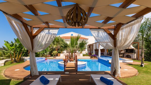 Área à beira da piscina com espreguiçadeiras, deck de madeira e vista para a piscina e uma casa.