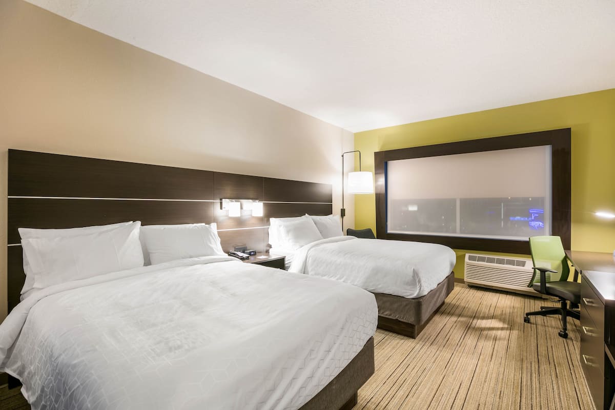 Habitación de hotel con dos camas, un escritorio, una silla y un amplio ventanal con vistas.