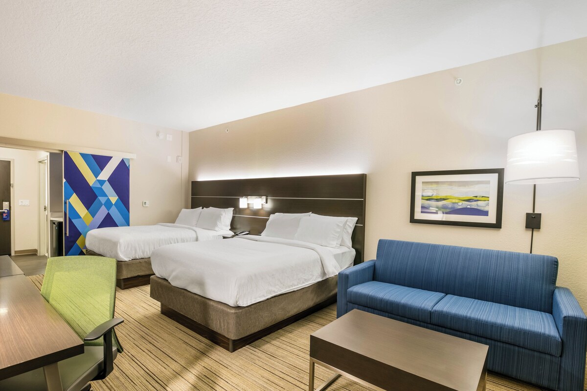Een hotelkamer met twee bedden, een blauwe bank, een kleine tafel en een schilderij aan de muur.