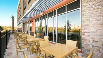 An outdoor seating area with tables and chairs, a stone wall, and a view of the water.