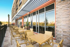 An outdoor seating area with tables and chairs, a stone wall, and a view of the water. - Holiday Inn Express & Suites Jacksonville - Town Center by IHG (Jacksonville)